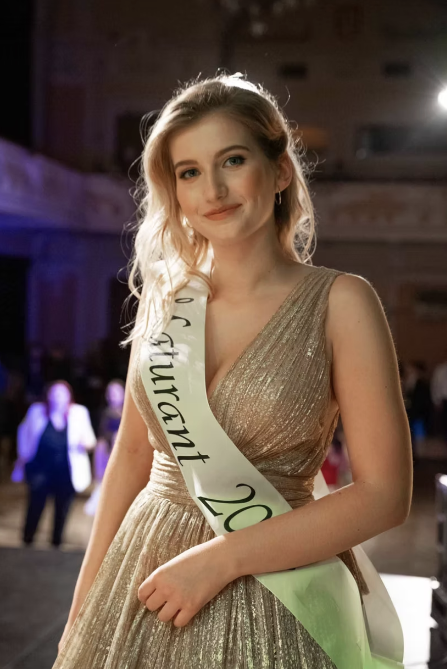 Mladá žena ve zlatých šatech se šerpou na plese
